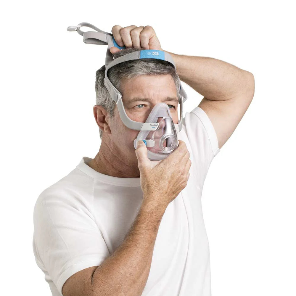 Man wearing a resmed f20 mask with headgear in white background for sleep apnea therapy