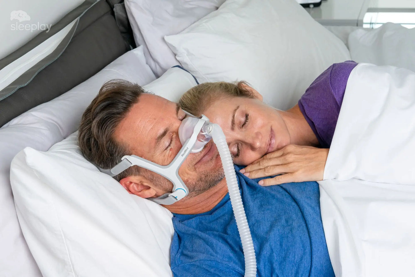 Man sleeping comfortably wearing a resmed n20 mask with tube, woman resting beside him in bed