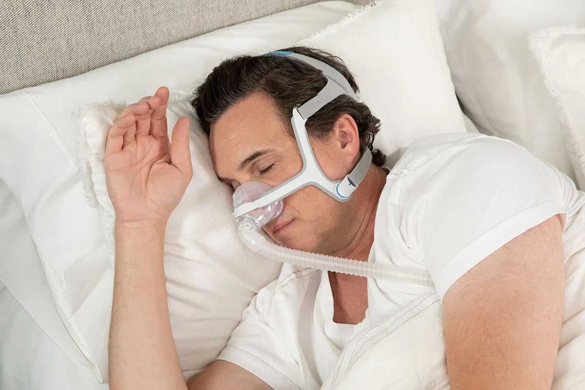 Man sleeping comfortably wearing a resmed n20 mask with headgear on a white pillow in bed