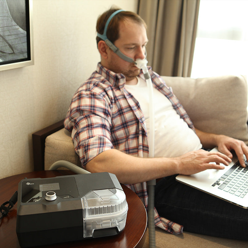 Man using G2S Auto CPAP system with nasal mask while working on laptop at home