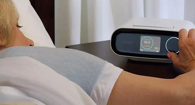 Person adjusting settings on Philips DreamStation BiPAP AVAPS 30 device placed on bedside table