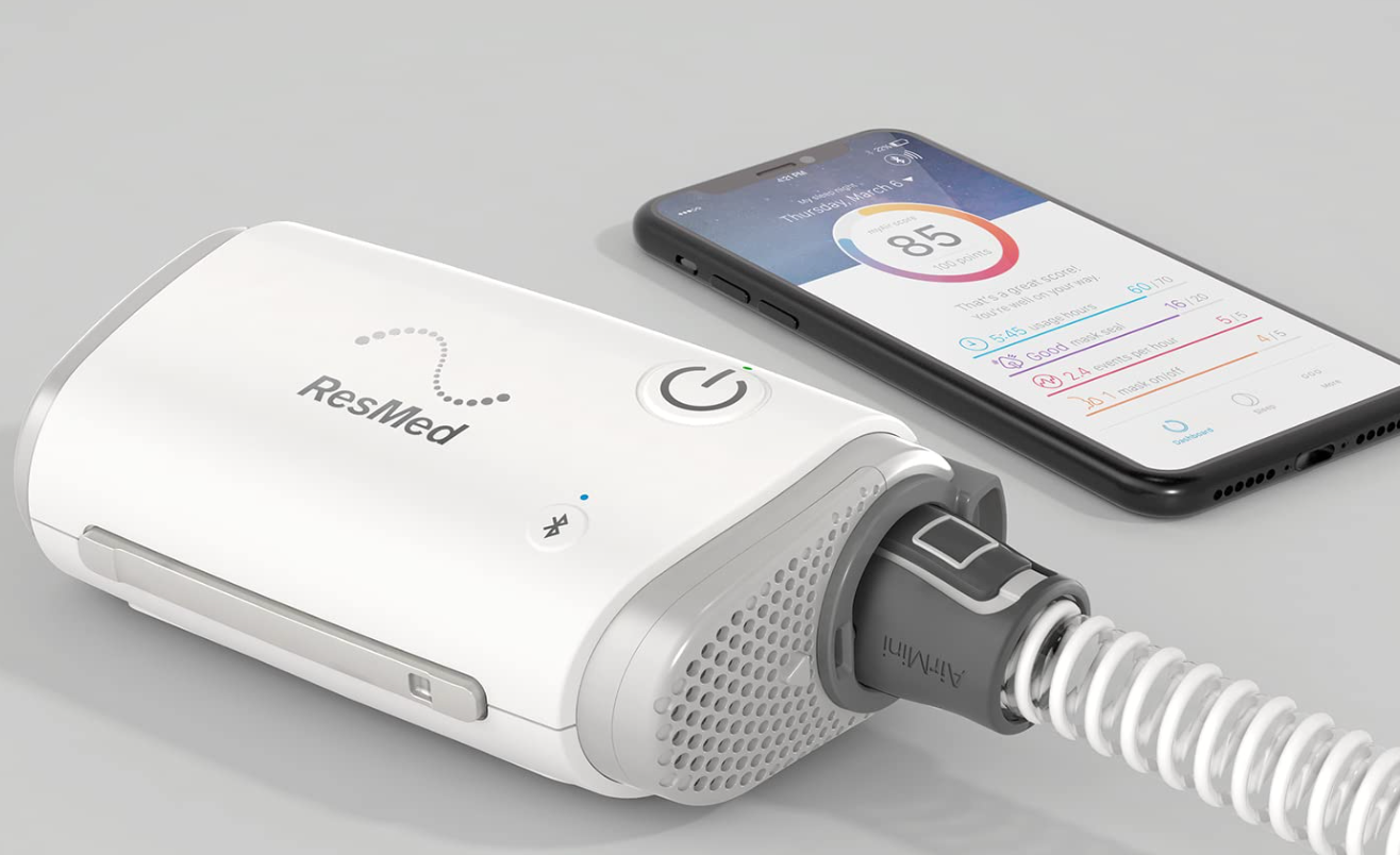 ResMed AirMini Portable Autoset compact CPAP device next to smartphone displaying sleep data