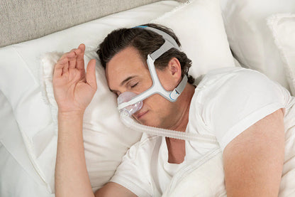 Man sleeping comfortably wearing a resmed n20 mask with headgear on a white pillow in bed
